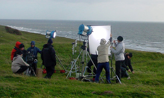 Ett filmteam står i blåst vid havet